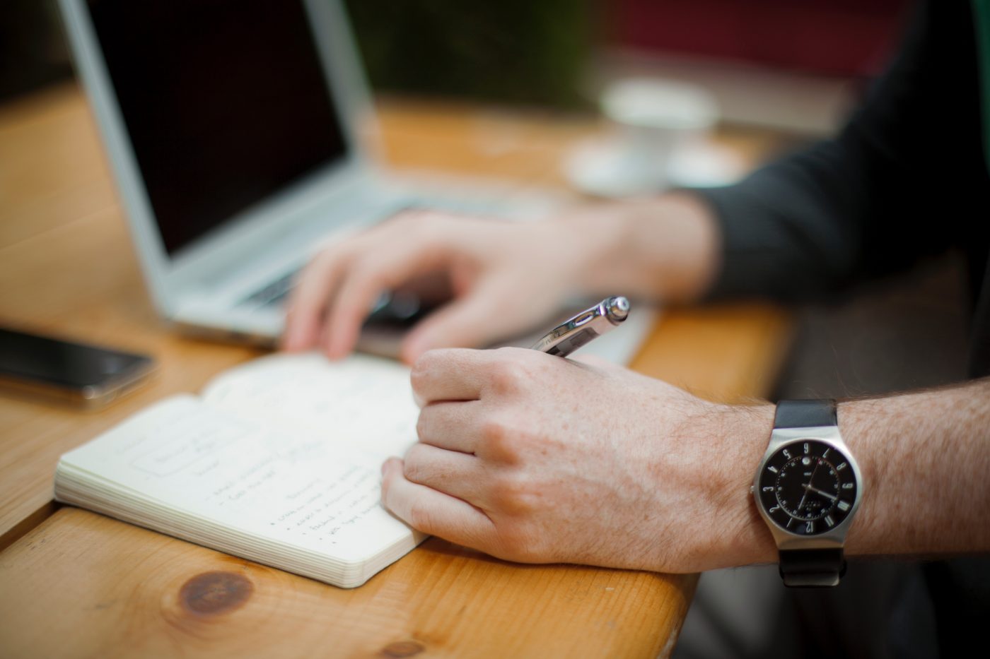 man with watch writing in notebook